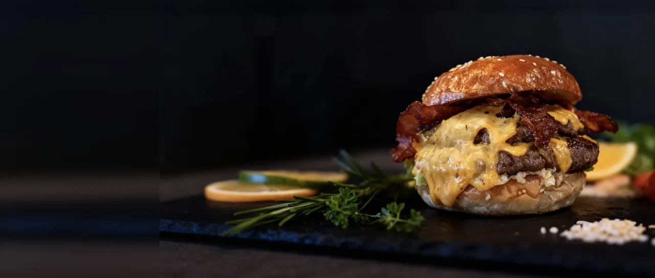 A bacon cheeseburger, enhanced by MenuPhotoAI from a real phone photo, on dark slate