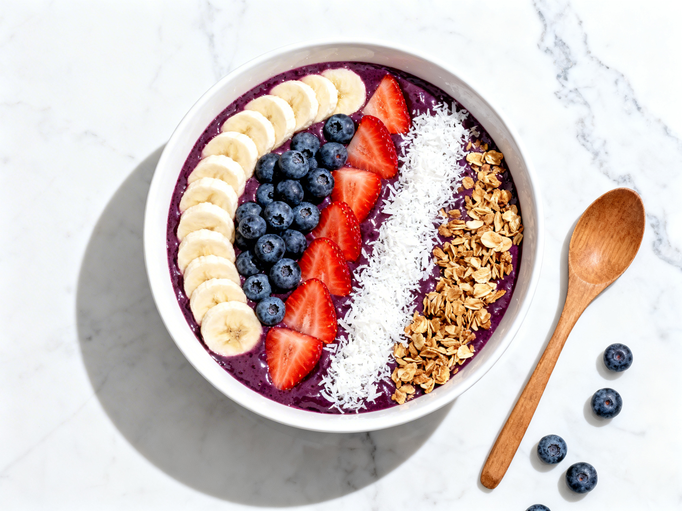 Acai bowl overhead at 90 degrees — deep-purple glossy base with strict topping zones of banana slices, blueberries, strawberries, coconut flakes, and granola on white marble