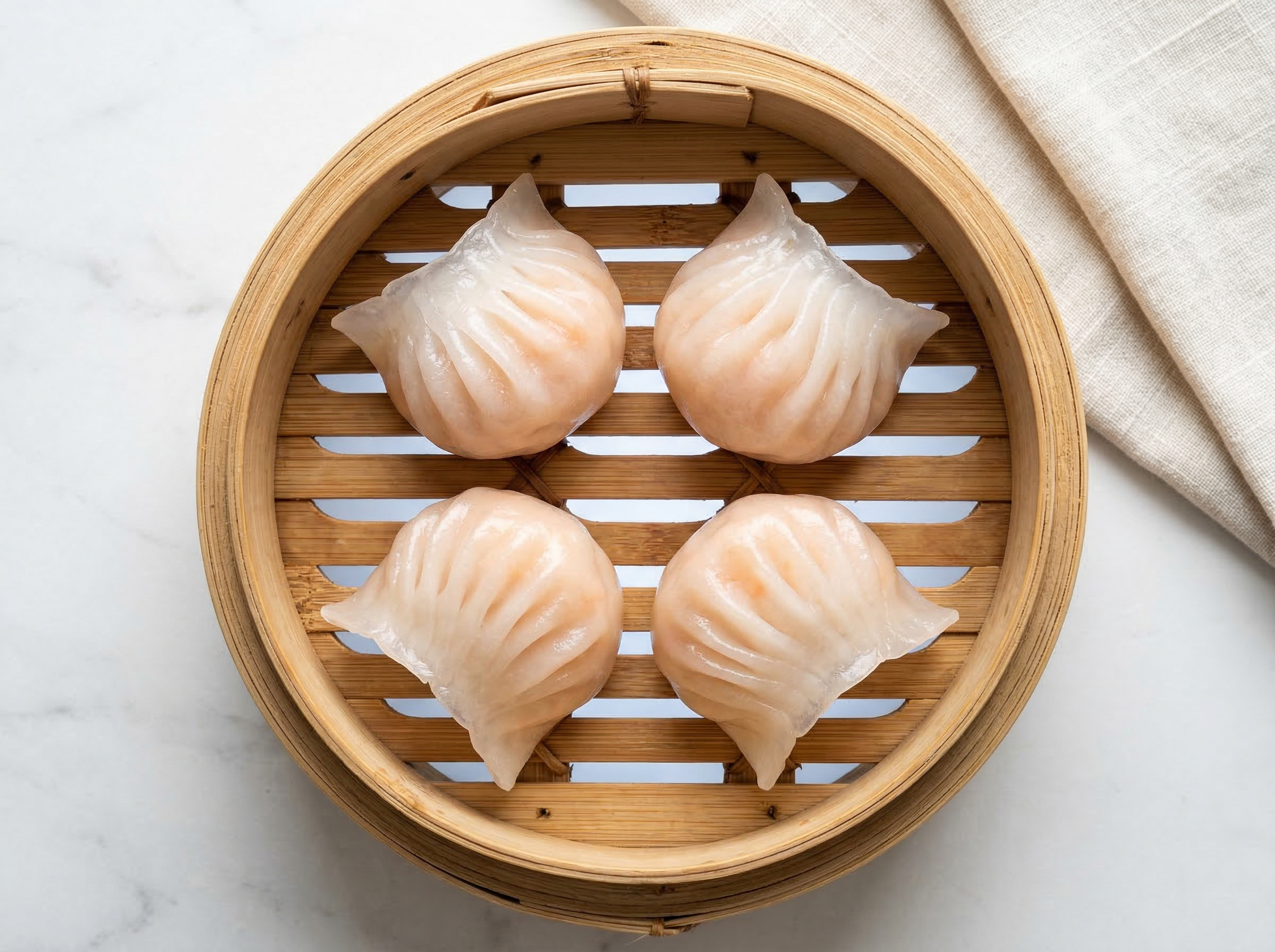 Har gow dumplings in open bamboo steamer basket backlit to show pink shrimp silhouette through translucent white wrapper skin, cool neutral light, single basket shot from overhead