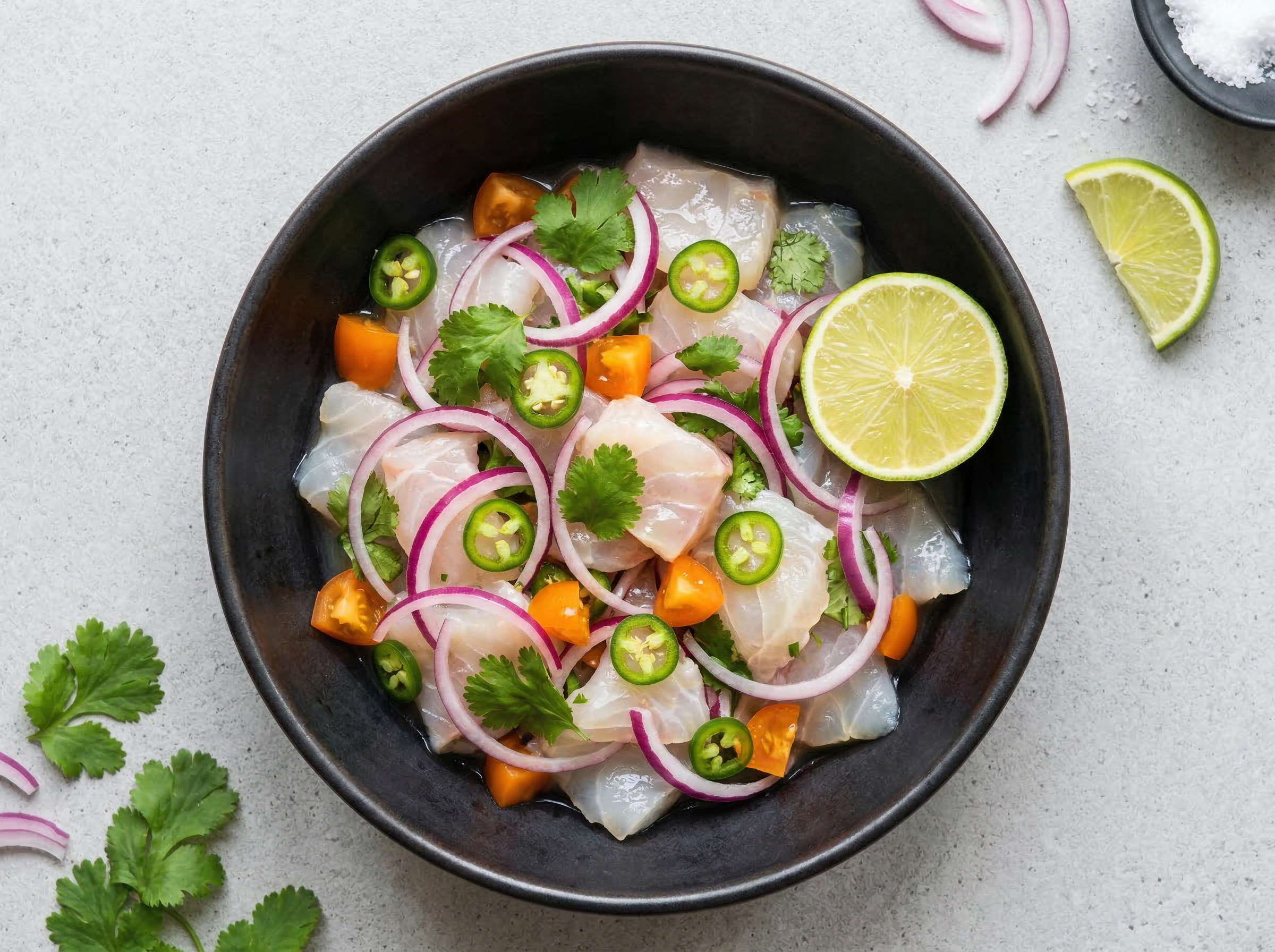 Ceviche in dark ceramic bowl overhead showing translucent white fish, red onion, cilantro, and lime against the dark bowl