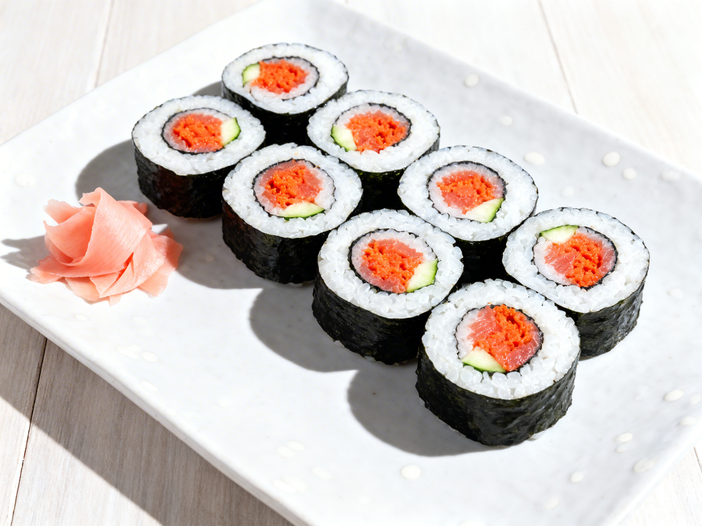 Six spicy tuna maki cross-sections arranged in a slight arc on a white ceramic plate, shot from 90° overhead — concentric rings of nori, sushi rice, and orange-red tuna filling fully visible